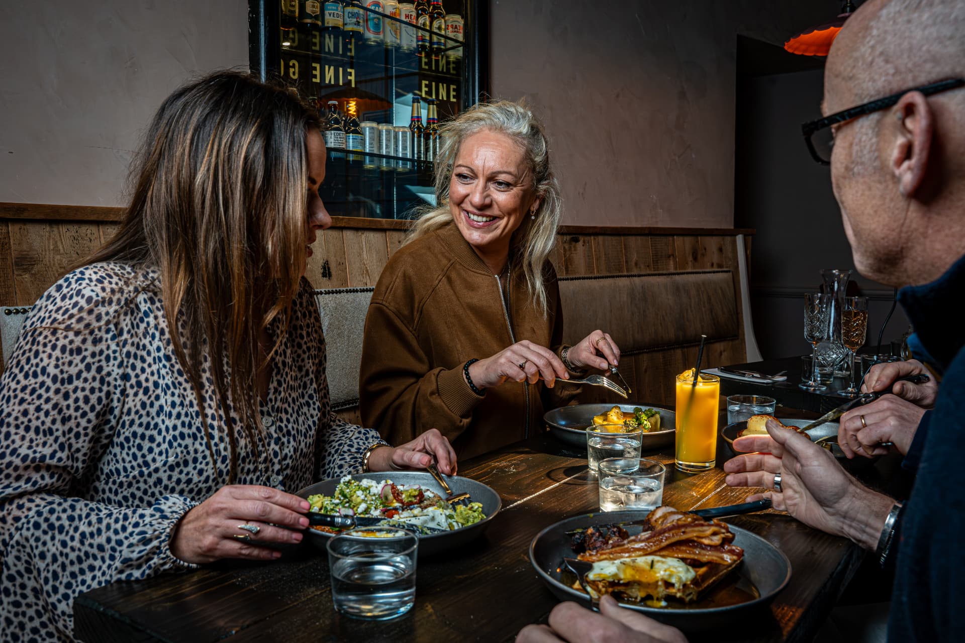 Friends laughing over brunch at a wooden table in a hotel restaurant