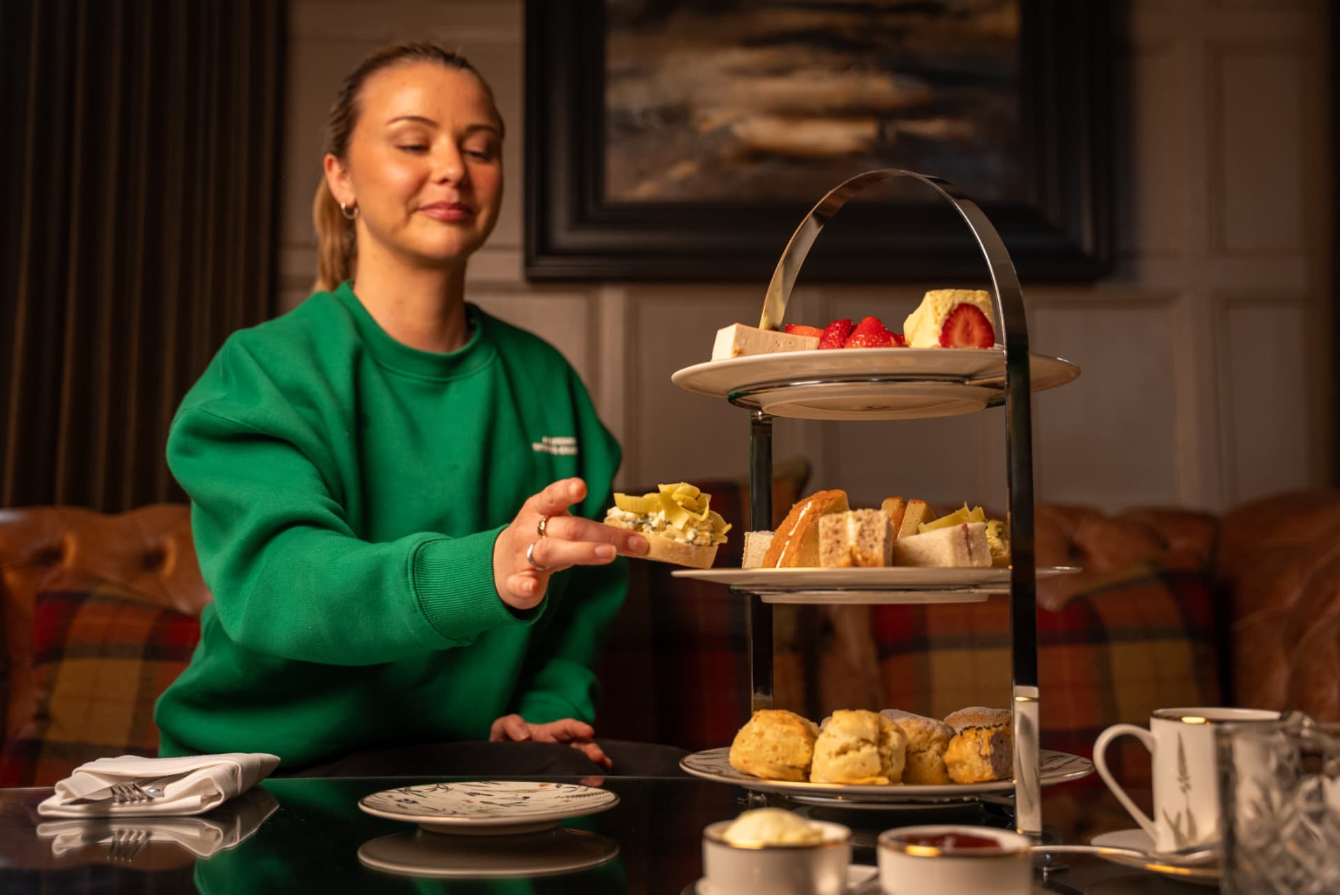 A guest choosing from an afternoon tea stand in a panelled hotel lounge