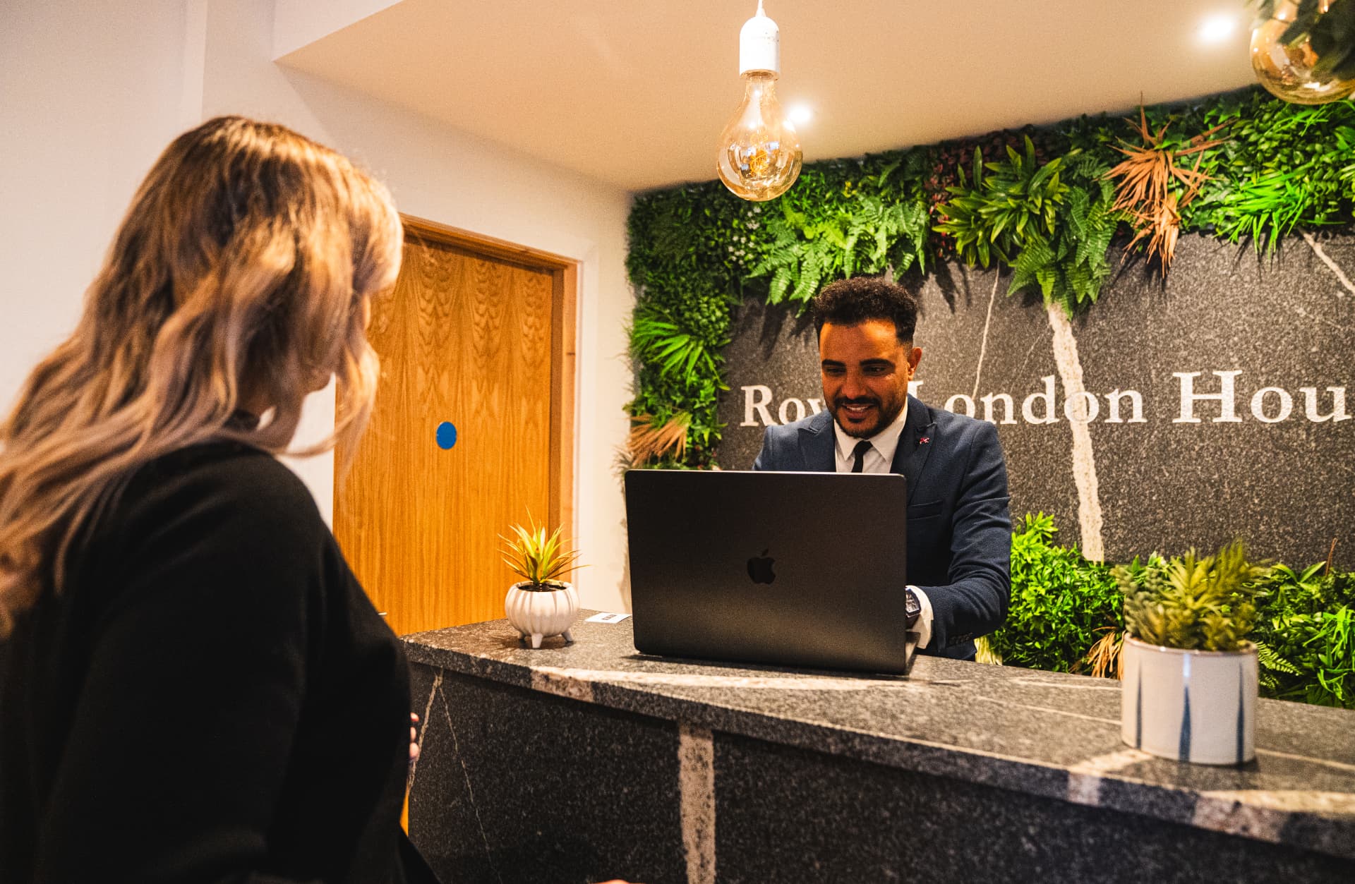 A guest being welcomed at a hotel reception desk with a living green wall