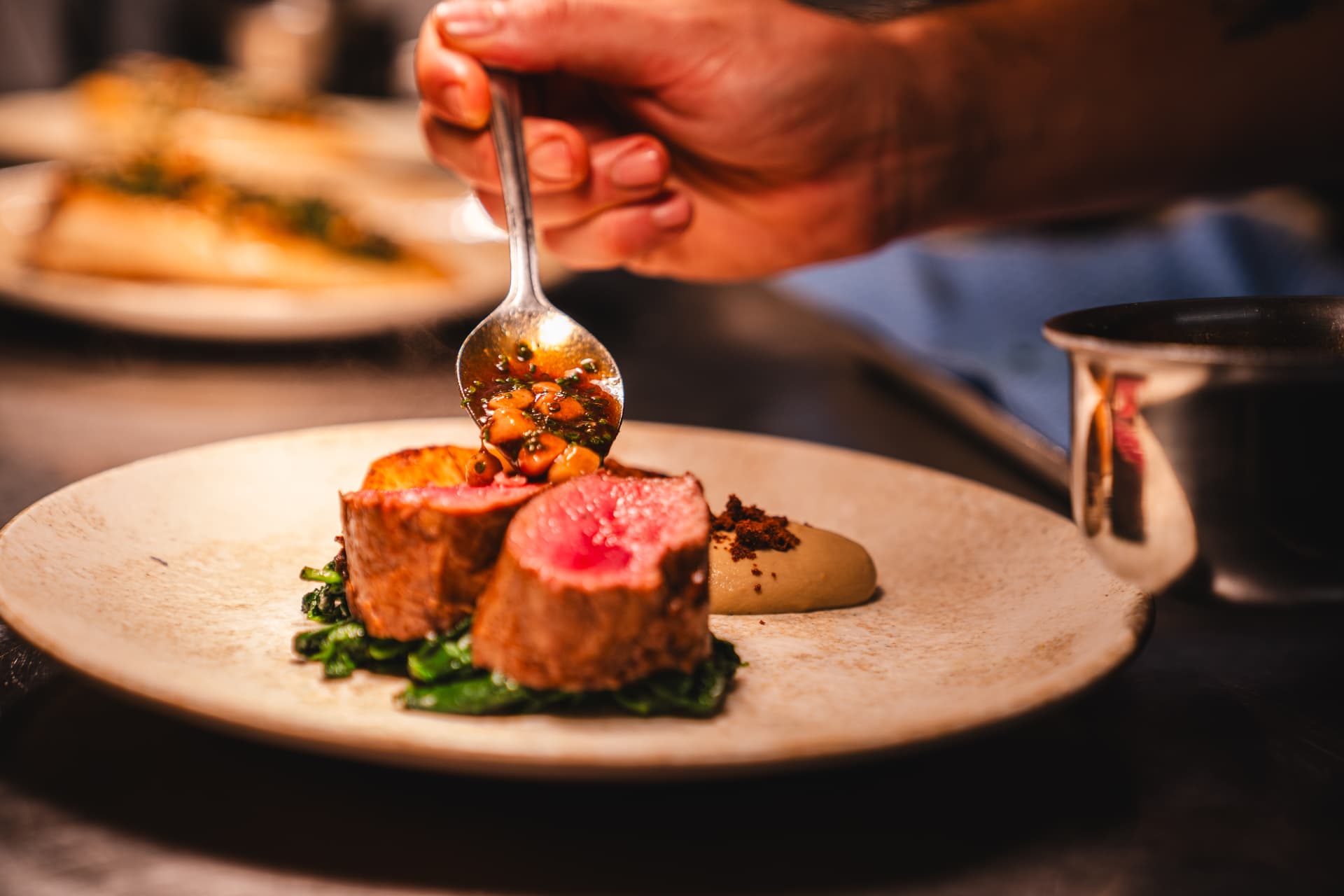Sauce being spooned over a plated dish in a restaurant kitchen