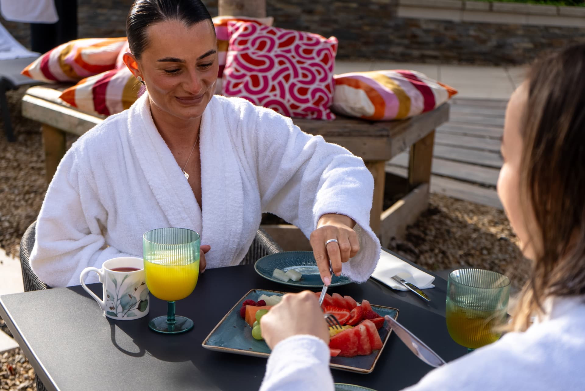 A guest in a white robe enjoying a fruit breakfast on a sunny spa terrace