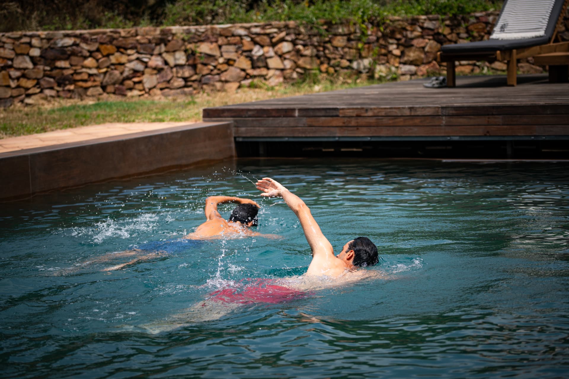 Two swimmers in a natural stone-edged pool at a rural retreat