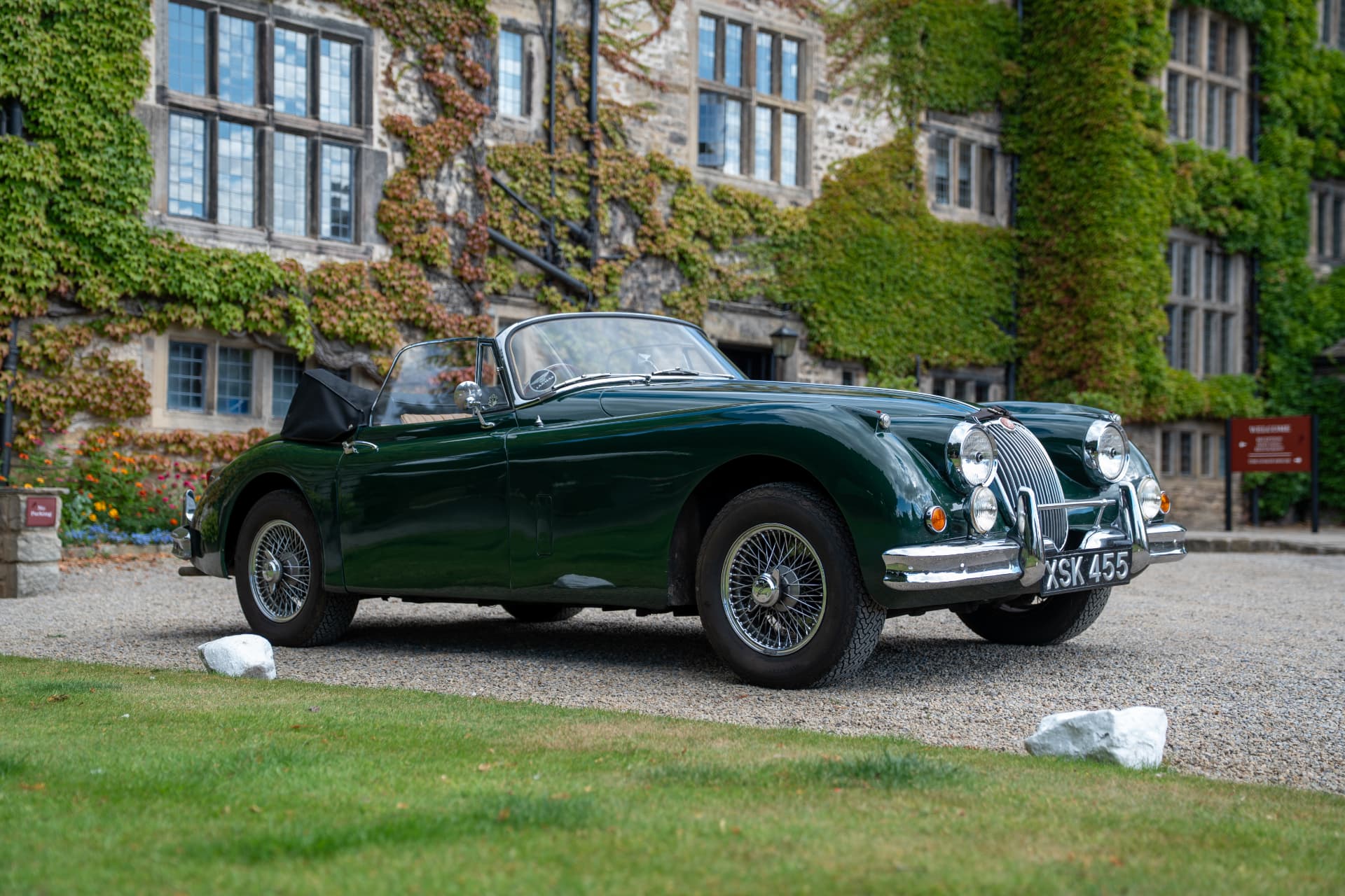 A classic green convertible parked before an ivy-covered country house hotel