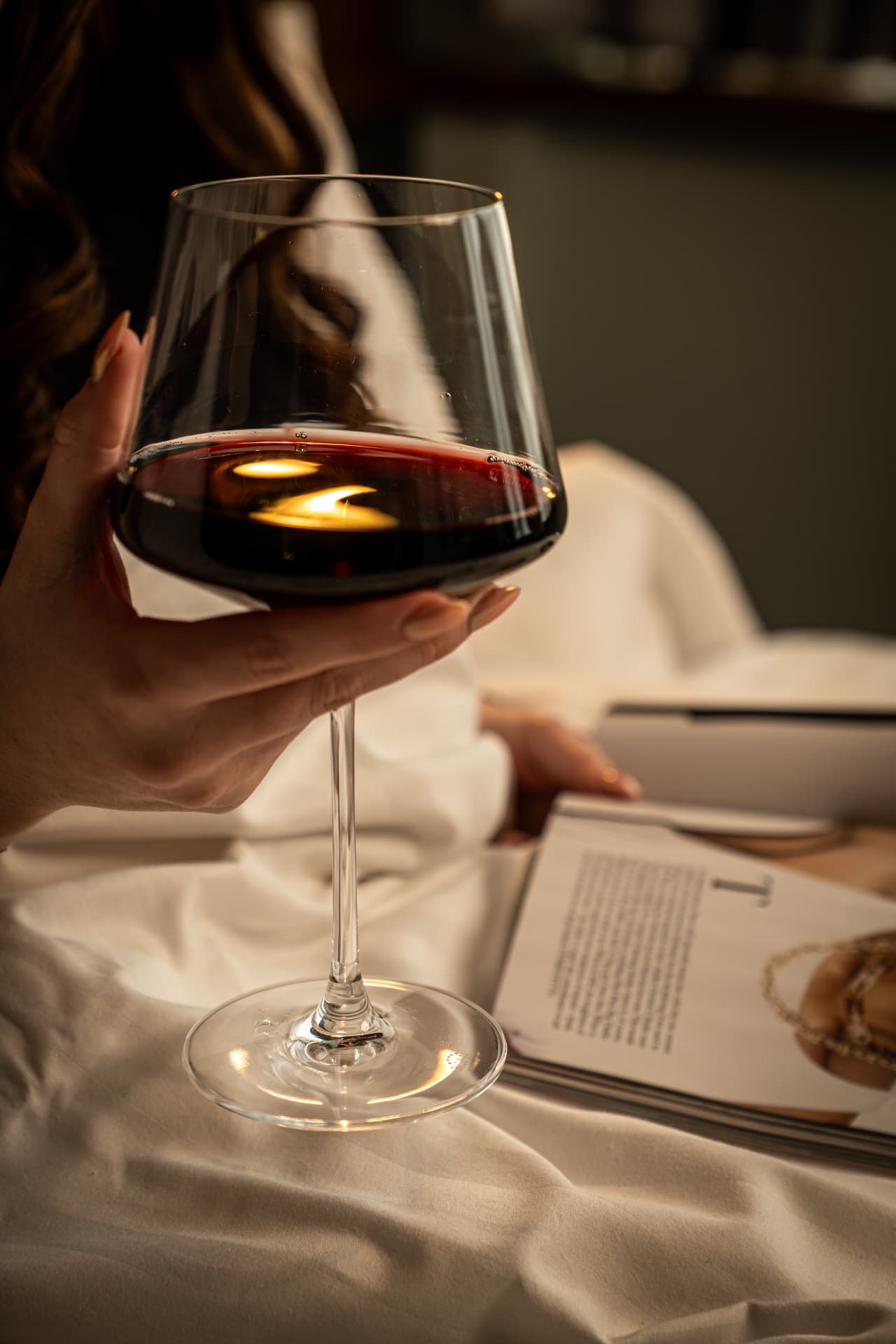 A glass of red wine held over a magazine on crisp hotel bed linen